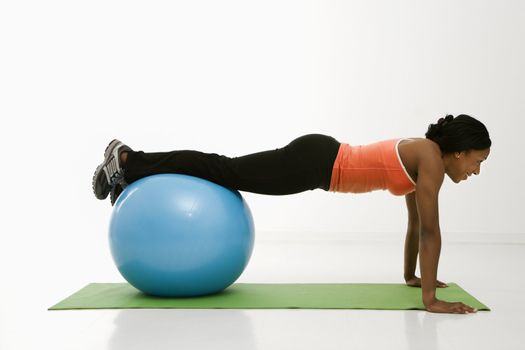 Profile of African American woman doing push ups with feet on exercise ball.