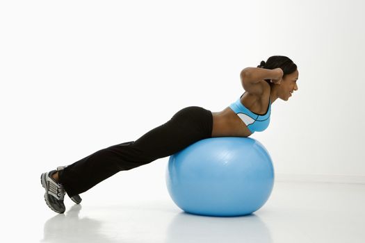 Profile of African American young adult woman working out with exercise ball.