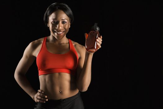 Smiling African American young adult woman holding water bottle with hand on hip.