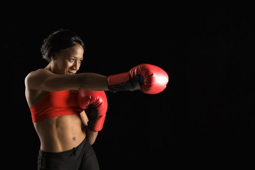 African American young adult woman wearing boxing gloves throwing punch.