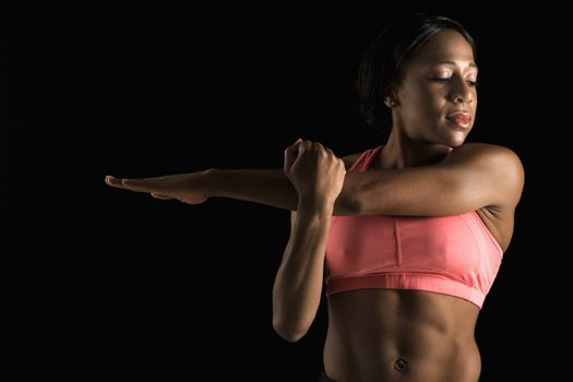 African American young adult woman in sports bra stretching arms with eyes closed.