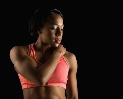 African American young adult woman in sports bra with hand on shoulder and eyes closed.