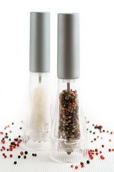 salt and pepper grinders on a table, with pepper spread around