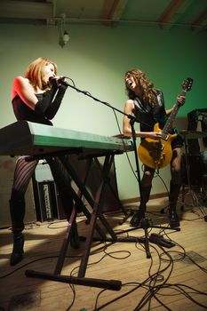 Two caucasian girls singing into microphone and playing the guitar.