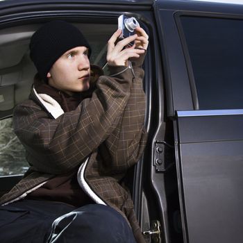 Caucasian male teenager taking a picture from his car.