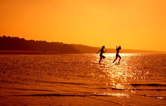 silhouette image of two running girls in water