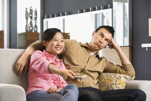 Asian couple sitting on couch watching TV.
