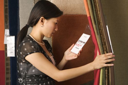 Asian female shopping rugs in retail store.