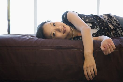 Portrait of Asian female lying on bed looking at viewer.