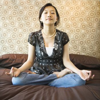 Asian female sitting on bed meditating.