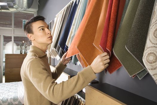 Asian male looking at fabric swatches in retail store.