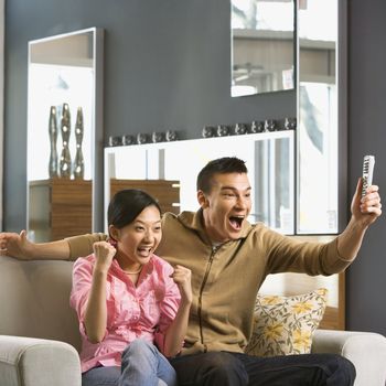 Asian couple cheering while watching television.