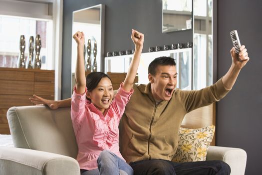 Asian couple cheering while watching television.