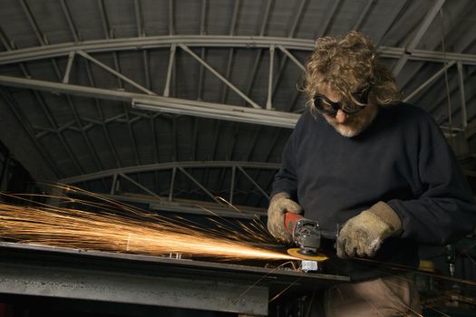 Caucasian male metalsmith shaping metal and creating sparks.