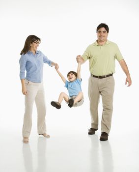 Hispanic mother and father swinging son against white background.