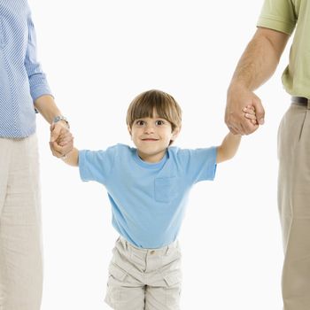 Boy holding hands with parents standing against white background.