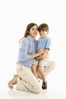 Mother kneeling down holding son against white background.