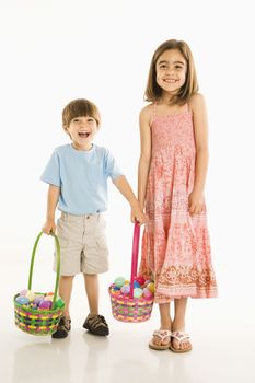 Smiling girl and boy standing with Easter baskets against white background.