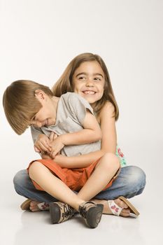 Boy sitting on girl's lap smiling against white background.