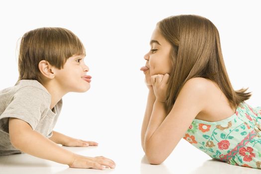 Portrait of girl and boy lying looking at eachother sticking out tongues.