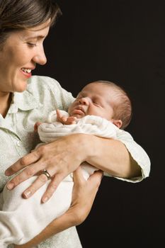 Mother smiling holding baby against black background.