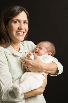 Mother smiling holding baby against black background.