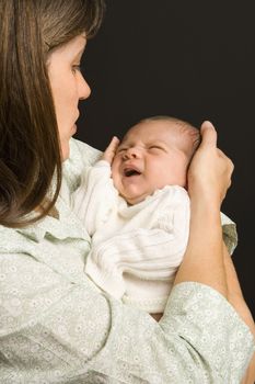 Mother smiling holding baby against black background.