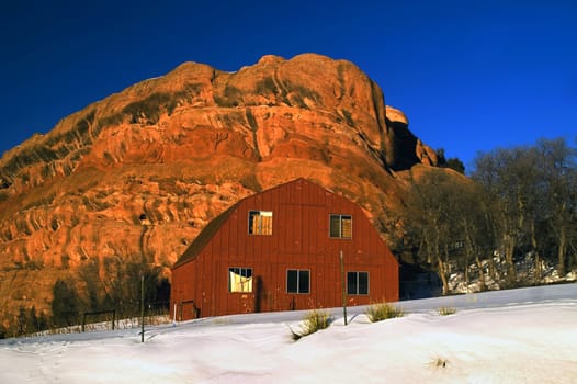 A rural red barn in Colorado winter snow showcasing the state's blue skies