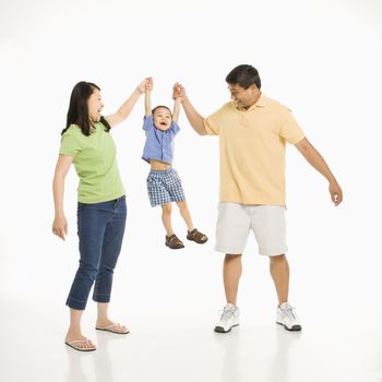 Asian mother and father holding hands with son and lifting him up in front of white background.