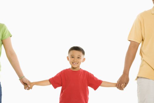 Asian parents holding hands with son in front of white background.