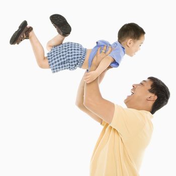 Asian father lifting son up into air in front of white background.