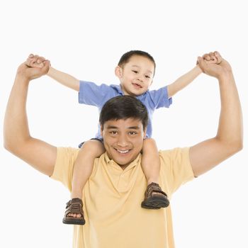 Asian father holding son on shoulders smiling in front of white background.