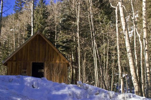 A old snow covered cabin with it's door open, seems to welcome visiitors to the cold Colorado snow in Winter