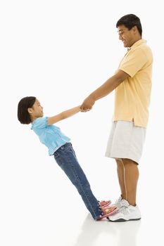 Asian daughter standing on father's feet holding his hands and leaning back.