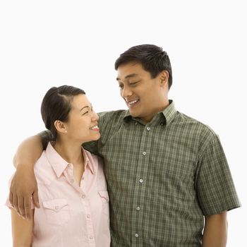 Mid adult Asian couple standing with arms around eachother and smiling at one another.