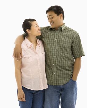 Mid adult Asian couple standing with arms around eachother and smiling at one another.