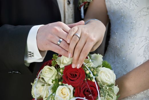 the bride and the groom showing their rings above the brides bouqet