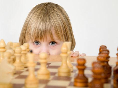Little girl peeps for game of chess on the white background
