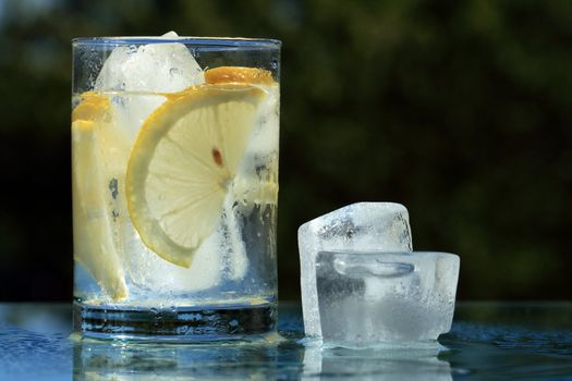 Glass of cold lemonade and ice cubes on dark background with copy space
