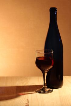 Wineglass near bottle of red wine with reverberation on brown background