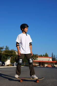 boy standing on a skateboard in an afternoon sun with blue sky in the background