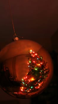 A reflection of a Christmas tree in a gold bauble ornament.
