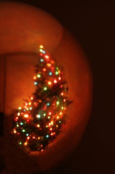 A reflection of a Christmas tree in a gold bauble ornament.
