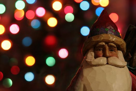A santa claus figurine with Christmas lights in the background.