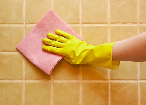 hand in yellow glove with rag, washing tiled wall