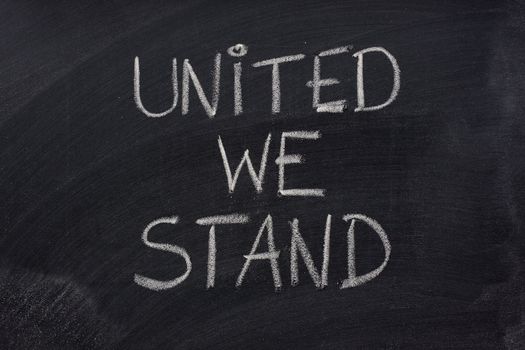 united we stand phrase handwritten with white chalk on blackboard