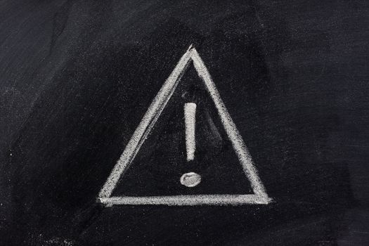 warning sign, exclamation mark inside a triangle, sketched with white chalk on blackboard