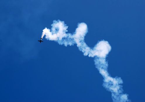 small plane in acrobatic flight with spiral trace over blue sky