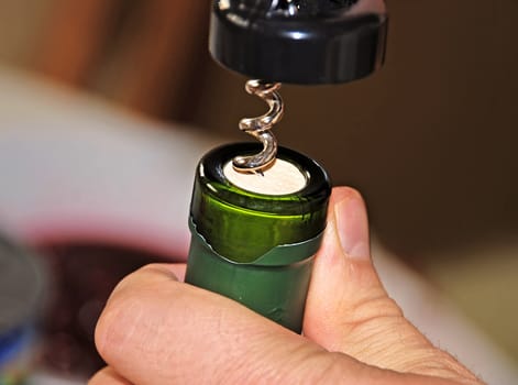 man hand opening green wine bottle with corkscrew closeup