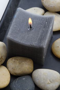 Dark grey candle in a plate with rounded rocks